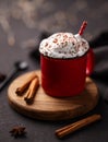 Red mug with hot chocolate or cocoa with whipped cream on a wooden stand with cinnamon sticks and star anise