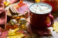 Red mug hot chocolate with marshmallows on table with maple leaves, garlands, cinnamon sticks. Autumn atmosphere, warming coffee,