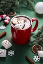 Red mug with hot chocolate and melted marshmallow snowman, green festive background