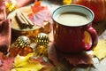 Red mug with hot cocoa on table with fallen maple leaves, round lamps, garlands, cinnamon sticks, warm blanket. Autumn atmosphere,