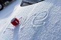 A red mug with a hot drink on a snowy car hood on a bright winter sunny day. The inscription on the snow is love. Selective focus Royalty Free Stock Photo