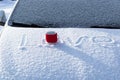 A red mug with a hot drink on a snowy car hood on a bright winter sunny day. The inscription on the snow is love. Selective focus. Royalty Free Stock Photo