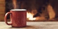 Red mug with hot tea in front of a burning fireplace, comfort, winter holidays and warmth of the hearth concept Royalty Free Stock Photo