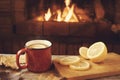 Red mug with hot tea with lemon in front of a burning fireplace, comfort and warmth of the hearth concept Royalty Free Stock Photo