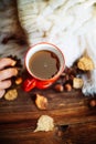 Mug of hot coffee in a woman's hand in a sweater in the autumn setting on a wooden table with a knitted scarf, sweater. Comfort, Royalty Free Stock Photo