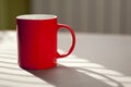 Red mug standing on a table against unfocused background.
