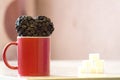 Red mug stands on the table, near the mug the heart shape of coffee beans, a symbol of love