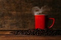 red mug with steam on a pile of fresh roasted coffee beans over wooden table Royalty Free Stock Photo