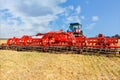 Universal red harrow as a hitch on an agricultural tractor against the background of a compressed yellow wheat field