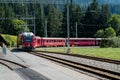 Red narrow gauge train arrives at a remote train station in the Swiss Alps Royalty Free Stock Photo