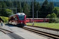 Red narrow gauge train arrives at a remote train station in the Swiss Alps Royalty Free Stock Photo