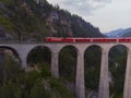 Red narrow gauge traincrossing over a stone bridge on a curvy stretch of track in the Swiss Alps.