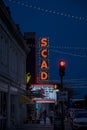 A red neon sign on the Savannah College of Art and Design with a marquee, people walking on the sidewalk, cars on the street