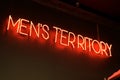 A red neon sign with the words mens territory hangs on the wall inside a salon