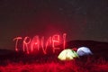 Red neon travel word. Two iluminated tents under stars at mountains at night