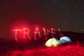 Red neon travel word. Two iluminated tents under stars at mountains at night