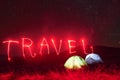 Red neon travel word. Two iluminated tents under stars at mountains at night