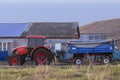 Red new wheeled tractor of medium size with blue trailer.