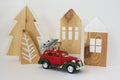Red New Year\'s car with a Christmas tree and gift boxes against the background of wooden toys in the Scandinavian style. Royalty Free Stock Photo