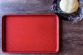 Red non-stick baking sheet, raw Russian Tea Cake cookie dough on plastic wrap and purple glass plate, dark wood table