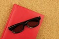 Red notebook and black glases on the cork board