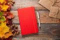 Red notebook with pen and paper envelopes on old wooden table. Mixed maple autumn leaves and acorns next to a closed notebook Royalty Free Stock Photo