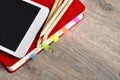 Red notebook and white tablet on a table with a wooden texture.