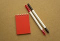 Red notepad for notes with red sheets. Blank space for notes. Mocap. Two felt-tip pens in red and black. On a warm ochre gray