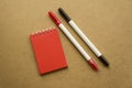 Red notepad for notes with red sheets. Blank space for notes. Mocap. Two felt-tip pens in red and black. On a warm ochre gray