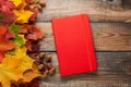 Red Notepad on old wooden table. Mixed maple autumn leaves and acorns next to a closed notebook