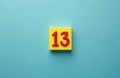 Red number thirteen rests on yellow square block against simple blue backdrop. Number 13 is centrally placed, creating focus on Royalty Free Stock Photo