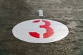 Red number three inside a white circle and an arrow painted on concrete Royalty Free Stock Photo