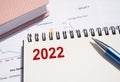 Red numbers 2022 in a white notepad on the office table next to a blue pen and pink organizer