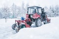 A red old tractor clears the street of snow in a snow storm. Street cleaning in winter Royalty Free Stock Photo