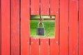 Red, old wooden fence texture background. Hole with hanging padlock with view on green, lush grass in the garden Royalty Free Stock Photo