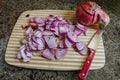 Red onions sliced on a wooden cutting board with a red handled knife and a whole onion on a marble countertop Royalty Free Stock Photo