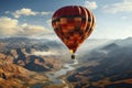 Red orange hot air balloon flies against a partly cloudy sky above a river through a beautiful valley with a backdrop of mountains Royalty Free Stock Photo