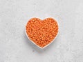 Red orange lentil Football in heart bowl on gray cement background