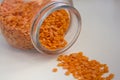 Red lentils are poured from a lying glass jar on a white background. Uncooked legumes close-up Royalty Free Stock Photo