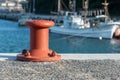 A red orange mooring bollard with a fishing boat in the background Royalty Free Stock Photo