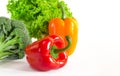 Juicy red and orange peppers with a green tail lies next to Bundle of lettuce and broccoli are on a white background Royalty Free Stock Photo