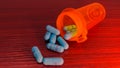 Red Orange Pill bottle overflowing with blue pills to show drug addiction and misuse for pharmaceutical drugs