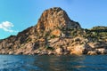 red orange stone rock, sharp mountain with green grass and tress stands on shore of Black sea on a bright sunny day