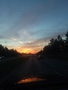 Red and orange sunset with wispy clouds above tree lined street