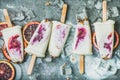 Red orange, yogurt, granola popsicles on ice cubes, concrete background