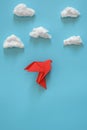 Red origami paper dove on a blue background among the white clouds