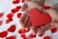 Red origami paper heart in male hands on a background of rose petals. Royalty Free Stock Photo