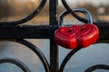 Red padlock is composition of two hearts hanging on black ornate railing of bridge fence on blurred river background Royalty Free Stock Photo