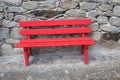 Red painted wooden bench standing on a stone pavement, rough wall with natural rocks