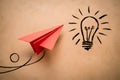 Red paper airplane flying next to hand drawn light bulb on beige background, symbolizing creativity and innovation
